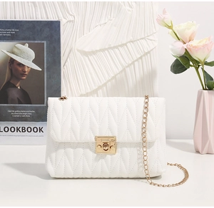 Detail of white wave-quilted crossbody bag with golden twist lock and elegant chain strap
