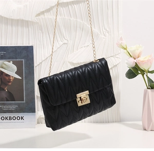 Detail of black V-quilted texture with golden chain strap and metallic lock on square bag