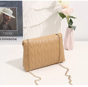 Close-up of beige quilted crossbody bag with delicate gold chain strap and V-shaped stitching