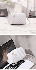 Detailed view of white quilted crossbody bag with V-shaped stitching and gold zippers