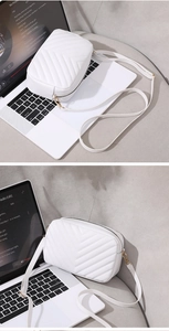 Close-up of white quilted camera bag with V-stitch details and gold zippers on a laptop