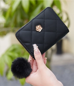 Detail of black quilted leather wallet with gold flower accent and fluffy pompom keychain