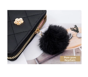 Detail of black quilted wallet with golden flower ornament and furry pom-pom charm
