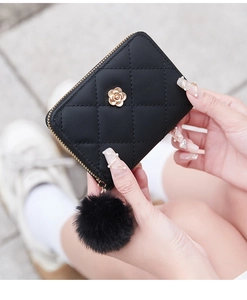 Detail of black quilted leather card wallet with gold camellia accent and pompom charm