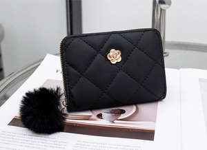 Close-up of black quilted wallet with gold camellia clasp and fluffy fur ball charm