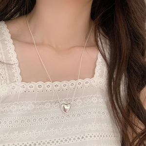 Polished silver heart pendant on a delicate snake chain worn on a lace background