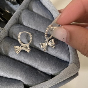 Détail de boucles d'oreilles nœud argenté avec texture perlée sur boîte à bijoux