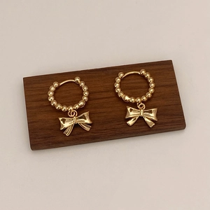 Vue détaillée de boucles d'oreilles dorées avec pendentif nœud sur bois sombre