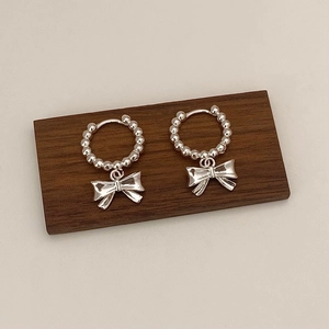 Détail de boucles d'oreilles nœud argentées avec anneaux perlés sur support bois