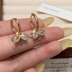 Gros plan de boucles d'oreilles lotus dorées avec zircons marquise tenus à la main