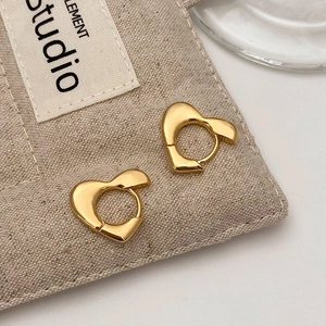 Detailaufnahme goldener, unregelmäßiger Herz-Ohrringe mit poliertem Finish auf Beigestoff