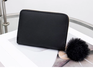 Close-up of black quilted short wallet with gold hardware and plush pom-pom charm