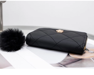 Detail of black quilted wallet with gold flower logo and fluffy pom pom keychain