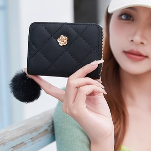 Black quilted short wallet with gold flower buckle and pompom charm held by hand