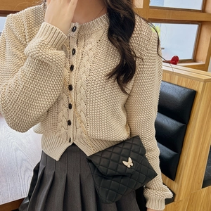 Beige Strickjacke mit Zopfmuster und schwarzen Knöpfen sowie gesteppter Kettenumhängetasche