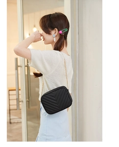 Close-up of black V-quilted camera bag with gold chain strap on a model shoulder