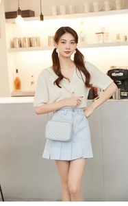 Light blue V-quilted camera bag with gold chain strap on a wooden counter detail