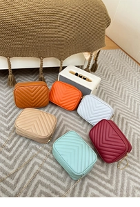 Flat lay of colorful chevron quilted crossbody bags with gold chain straps on a textured rug