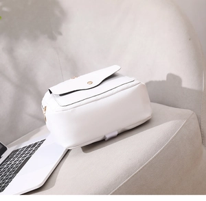 Detailed close-up of cream quilted crossbody bag with gold buckle on a soft chair