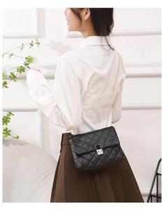 Detail of elegant black quilted crossbody bag with golden chain strap and twist lock