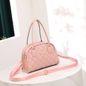 Detailed shot of pink quilted handbag with gold hardware and woven strap on marble stand