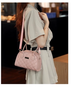 Detailed close-up of a pink quilted crossbody bag featuring a wide woven strap and gold hooks