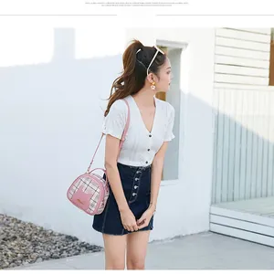Pink checkered crossbody bag with cat ear design on a model in bright outdoor sunlight