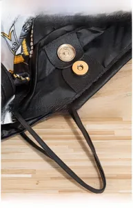 Close-up of high-polish gold magnetic closure and black textured leather detail on a tote bag