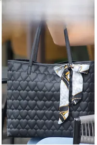 Detail of black heart-quilted tote bag featuring a decorative printed silk scarf handle