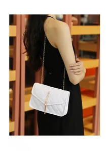 White quilted crossbody bag with gold chain strap and tassel detail on a female model