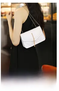 Close-up of white quilted crossbody bag with gold chain strap and tassel detail
