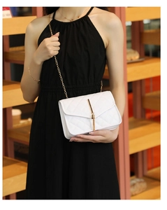 White quilted crossbody bag with gold chain strap and tassel detail on a female model