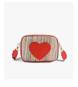 Detail of colorful woven straw bag featuring red heart patch and premium metal hardware