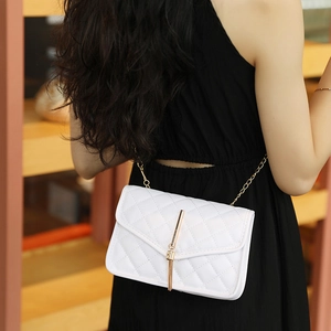White quilted crossbody bag with gold tassel and chain strap on a black dress