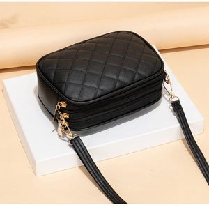 Detail of black quilted crossbody bag featuring triple zipper compartments and gold hardware