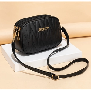 Detail of black quilted crossbody bag with golden metal logo and wave stitching pattern