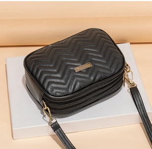 Detail of black quilted faux leather crossbody bag showing three zipper compartments