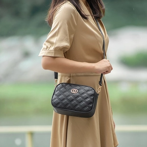 Classic black quilted crossbody camera bag with gold hardware worn by a model outdoors