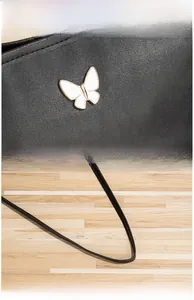 Détail de la boucle papillon dorée et fine bandoulière en cuir sur sac noir matelassé