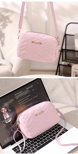 Pink wave-quilted crossbody camera bag with gold logo on a laptop in a cozy scene