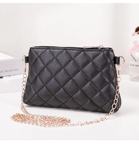 Détail du sac à bandoulière matelassé noir avec chaîne dorée sur un bureau blanc