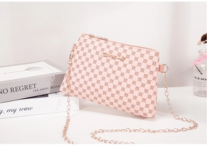 Détail d'un sac bandoulière rose avec imprimé pois, chaîne dorée et logo en métal