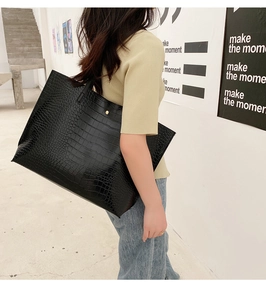 Détail d'un grand sac cabas noir motif crocodile avec boucle dorée porté par un mannequin