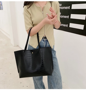 Détail d'un sac cabas noir à texture crocodile avec un fermoir magnétique doré