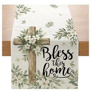 Close-up of floral table runner with wooden cross and 'Bless this home' text on linen