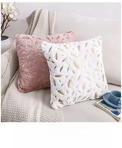 Detail of pink and white plush pillows with gold feather pattern on a white sofa