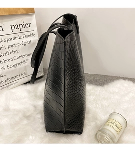Détail du sac cabas noir à motif crocodile sur tapis en peluche blanc avec accessoires