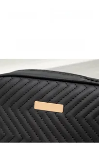 Detail of black quilted leather camera bag with V-shaped stitching and gold metal plate