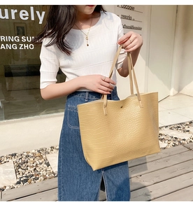 Détail du sac cabas beige à motif crocodile avec boucle en métal porté par un mannequin