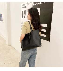 Gros plan d'un sac cabas noir à motif crocodile porté par un mannequin en extérieur